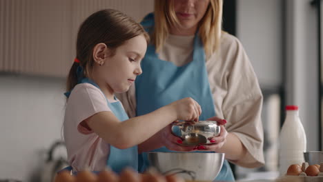 cute-and-curious-little-girl-is-helping-to-her-mother-in-kitchen-pouring-sugar-in-bowl-happy-childhood